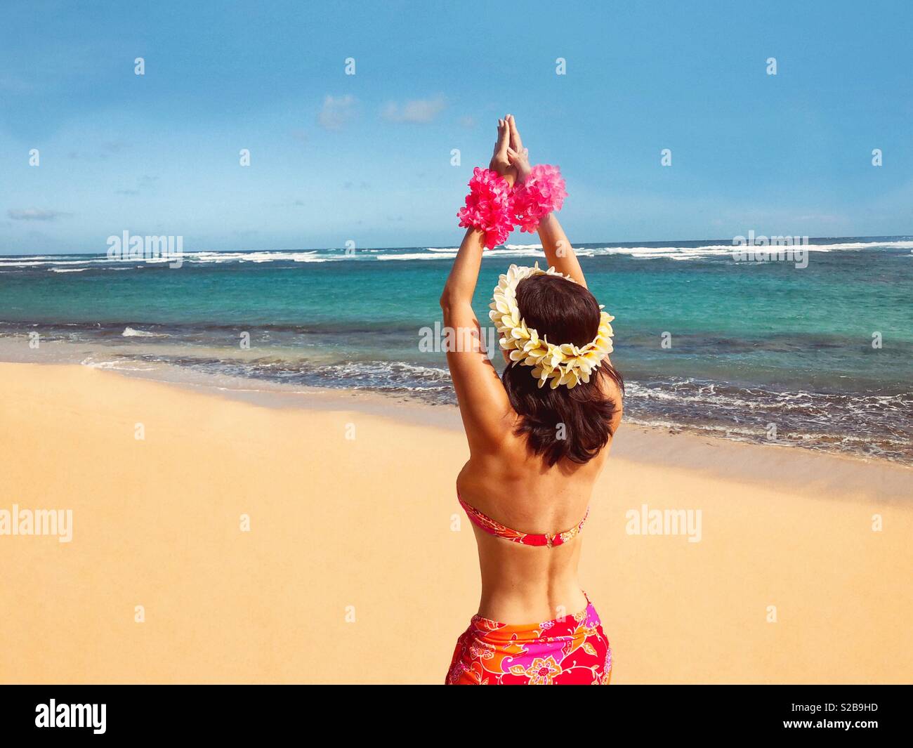 Native Hawaiian princess hula dancer on deserted Pacific island beach adorned with floral bikini and matching pareo, flowers, flowered leis in hands and hair Stock Photo