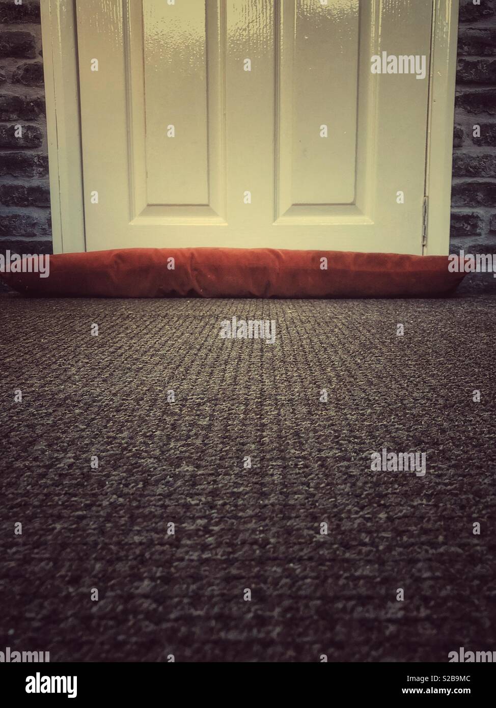 A draft excluder up against a creamy white door. To help keep the draft down from under the door. - Smartphone Captured Stock Image