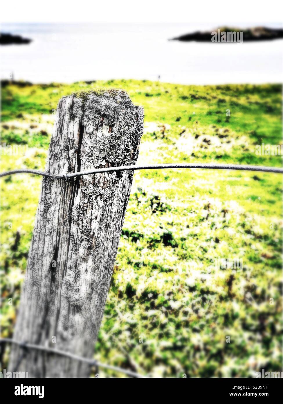 Weathered fence post looking on to island in small Western Isles Bay in Scotland in September - Smartphone Captured Stock Image