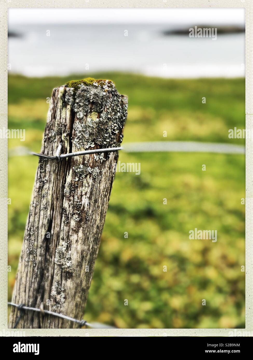 Weathered fence post looking on to island in small Western Isles Bay in Scotland in September - Smartphone Captured Stock Image