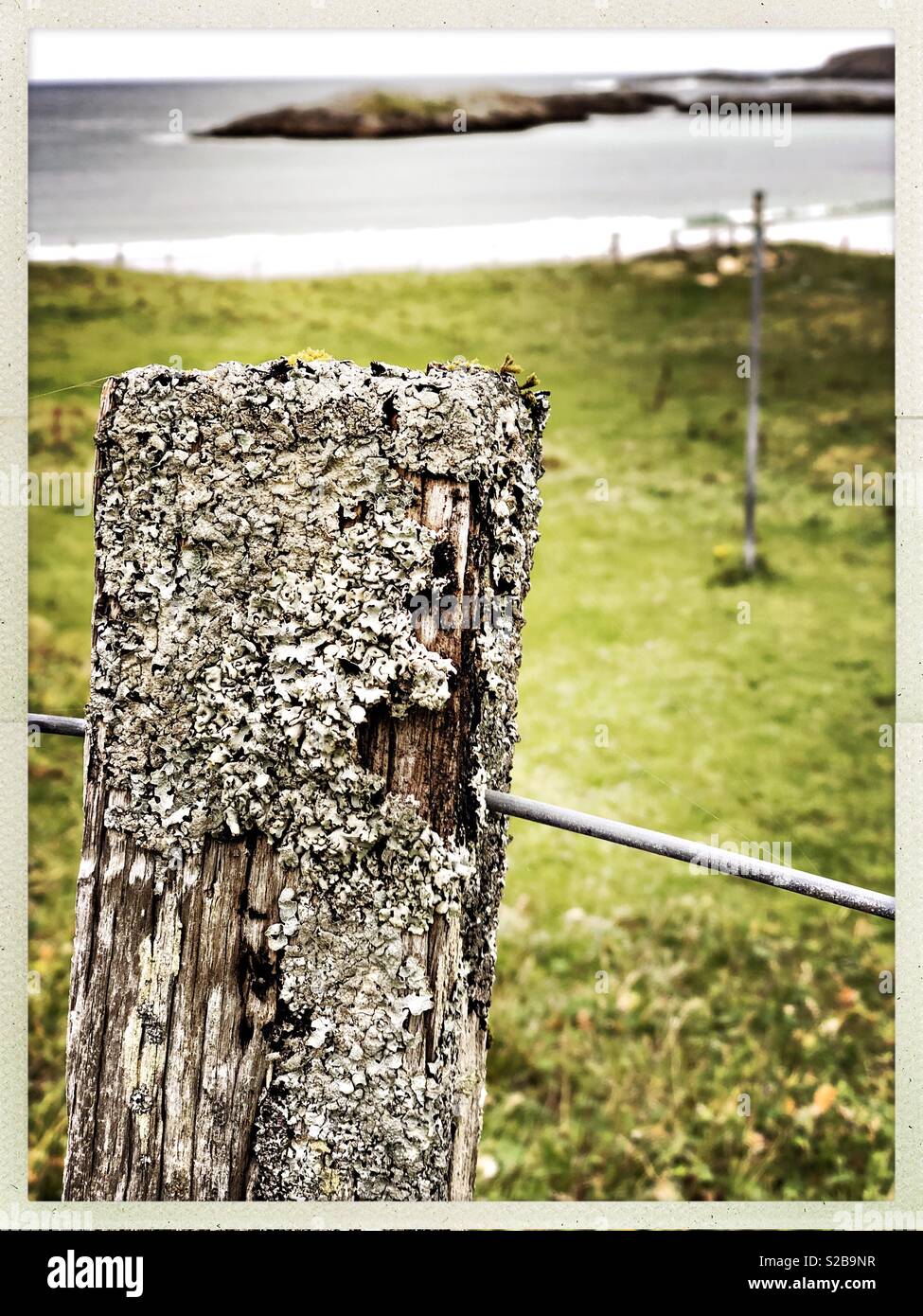 Weathered fence post looking on to island in small Western Isles Bay in Scotland in September - Smartphone Captured Stock Image