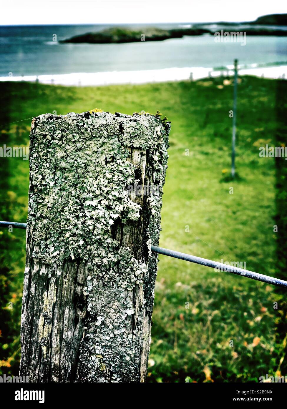Weathered fence post looking on to island in small Western Isles Bay in Scotland in September - Smartphone Captured Stock Image