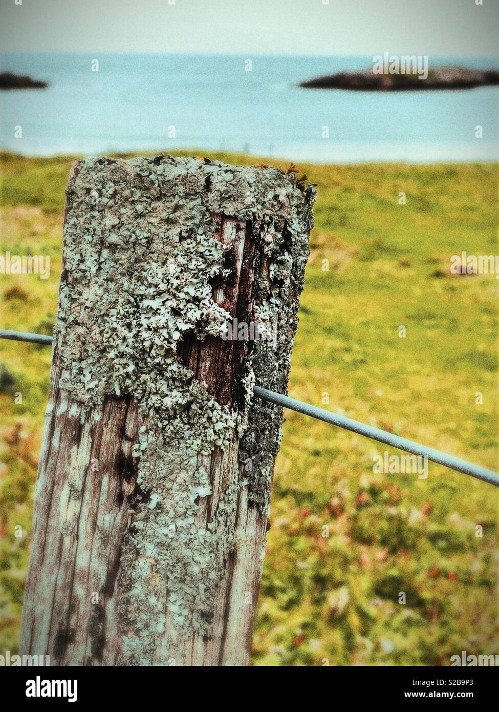 Weathered fence post looking on to island in small Western Isles Bay in Scotland in September - Smartphone Captured Stock Image