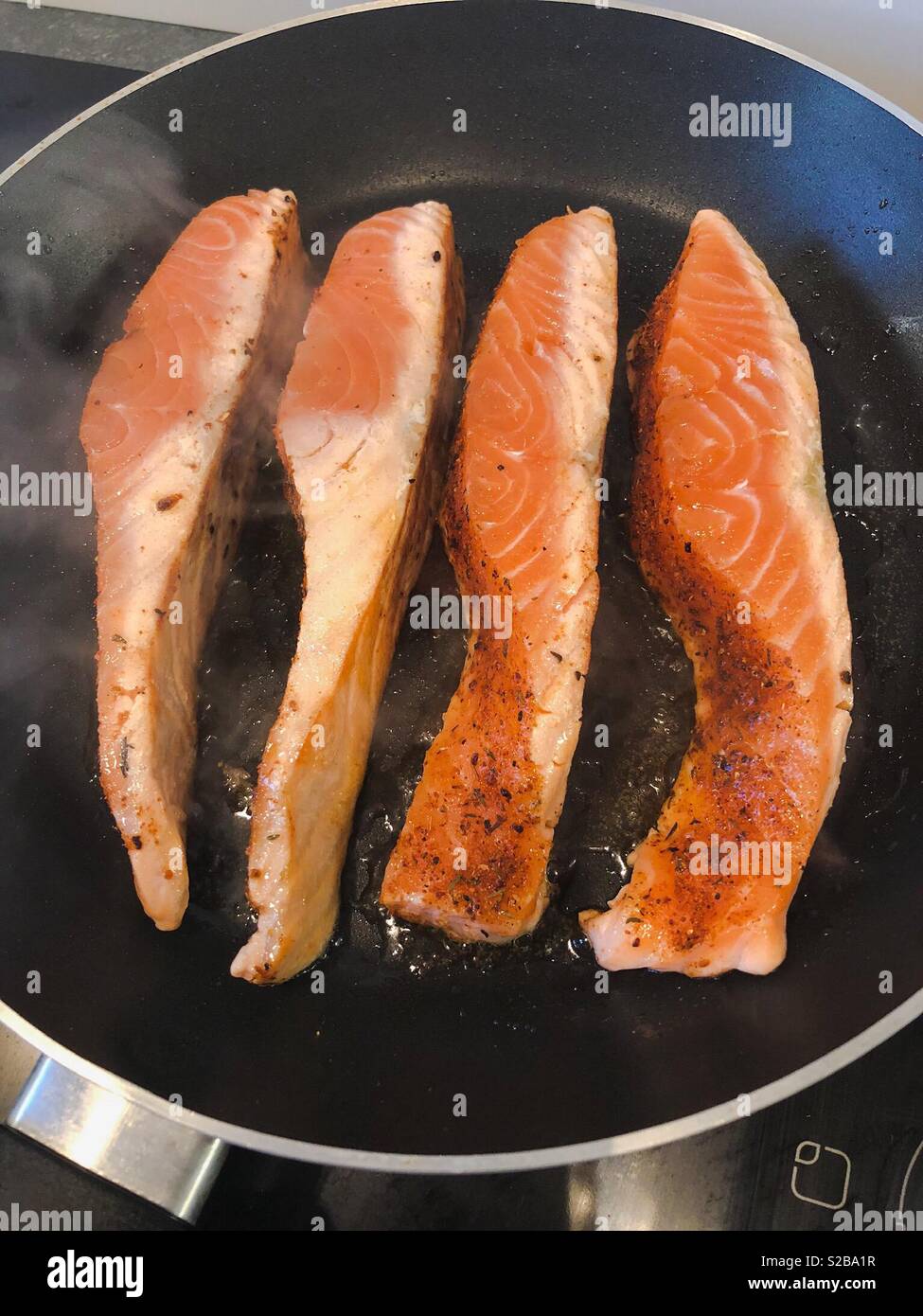 Four portions of salmon frying in a pan - Smartphone Captured Stock Image