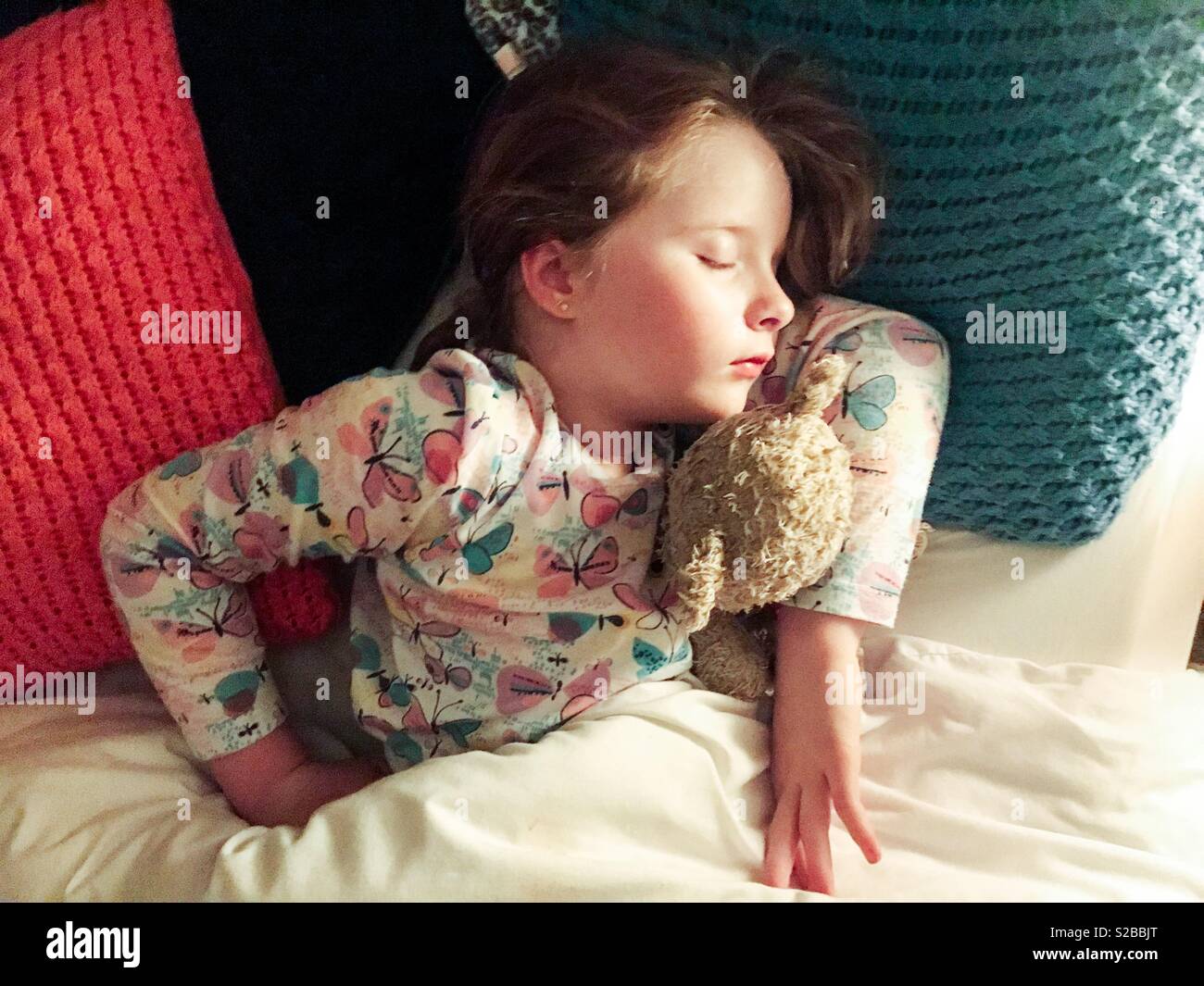 Young girl asleep in bed cuddling teddy bear Stock Photo