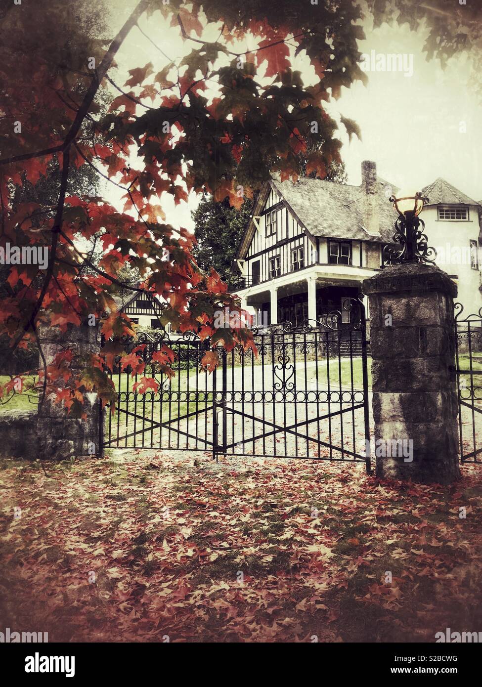 Red autumn leaves frame the iron gated entry to an older spooky home.  Moody, haunted Autumn concept Stock Photo