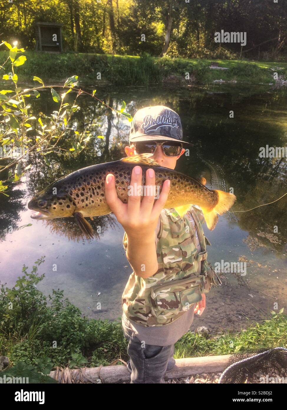 Nine-year-old boy with a brown trout, Church Paddock Trout fishery, Winchester, Hampshire, England, United Kingdom. - Smartphone Captured Stock Image