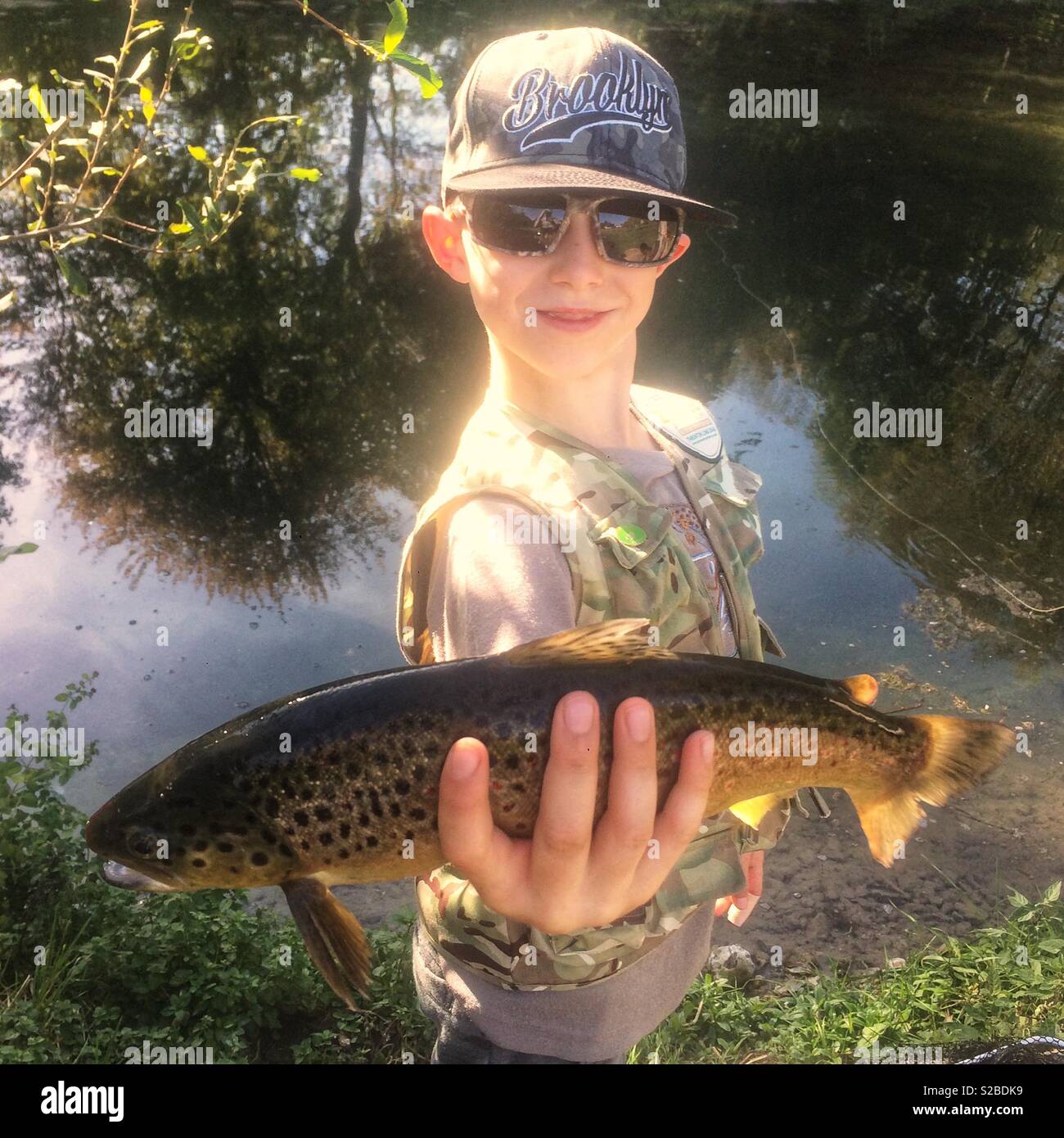 Nine-year-old boy holding a brown trout fish, Winchester, Hampshire, England, United Kingdom. - Smartphone Captured Stock Image