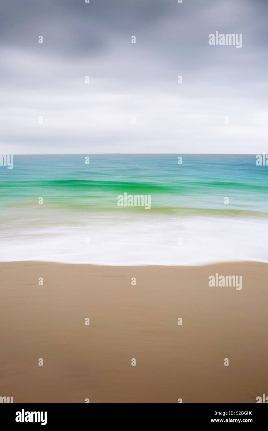 An abstract nature background of a sandy beach with white surf from an emerald green ocean under a cloudy sky with a blurred motion effect - Smartphone Captured Stock Image