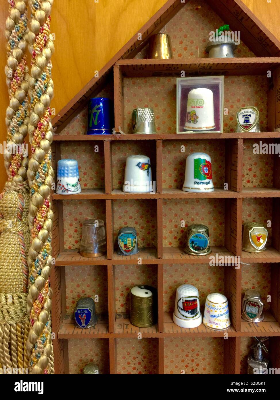 Thimble collection on a shelf made for souvenir thimbles with a gold corded rope. Stock Photo