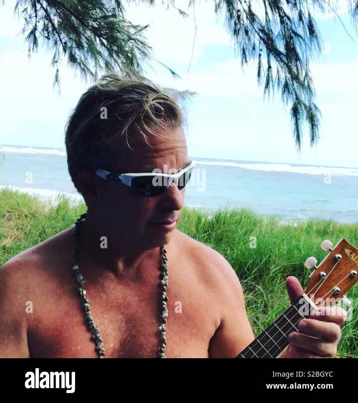 Man playing ukulele outside under a tree by the beach in Hawaii - Smartphone Captured Stock Image