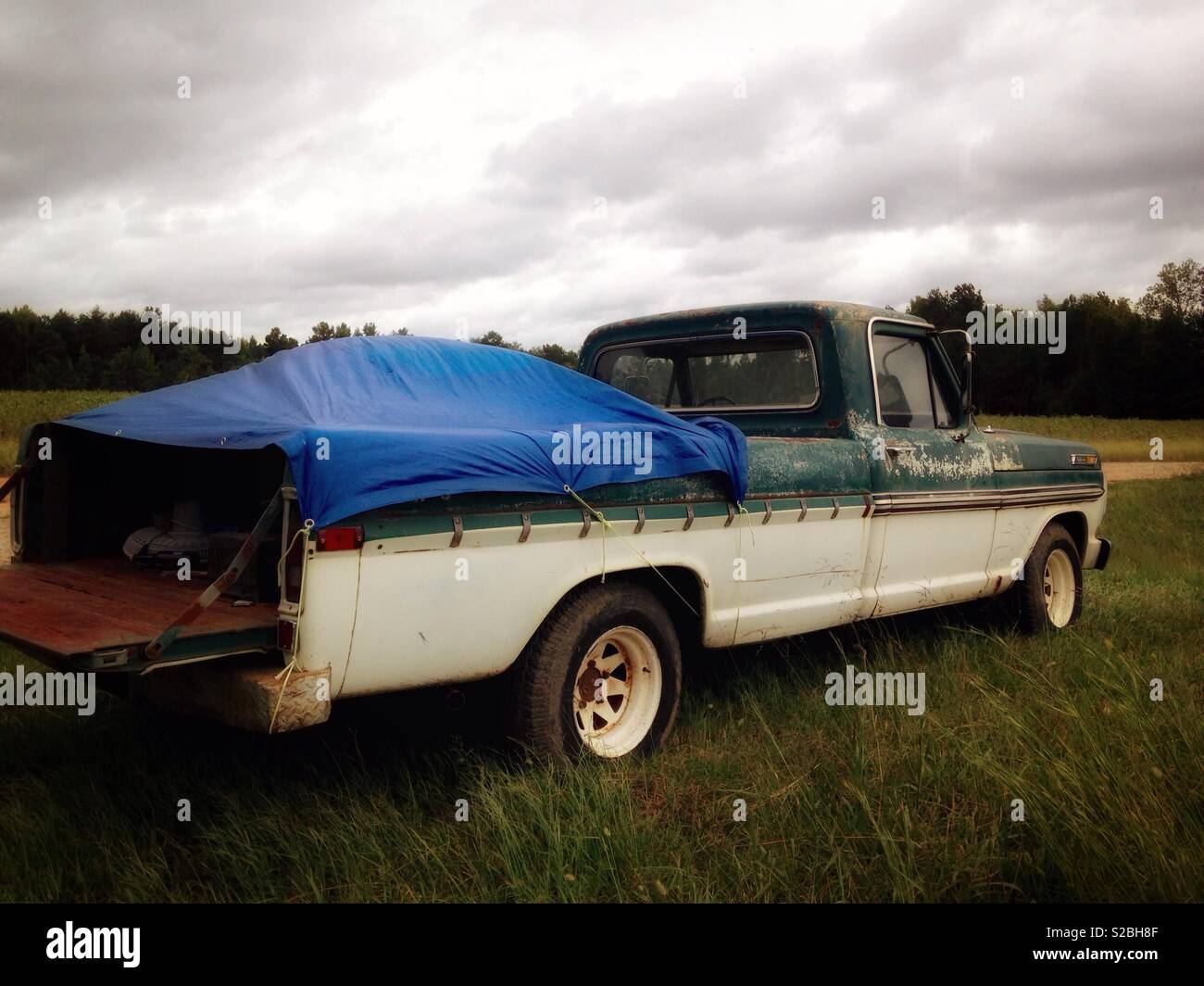 Vintage green and white Ford Ranger in farm field with overcast sky
