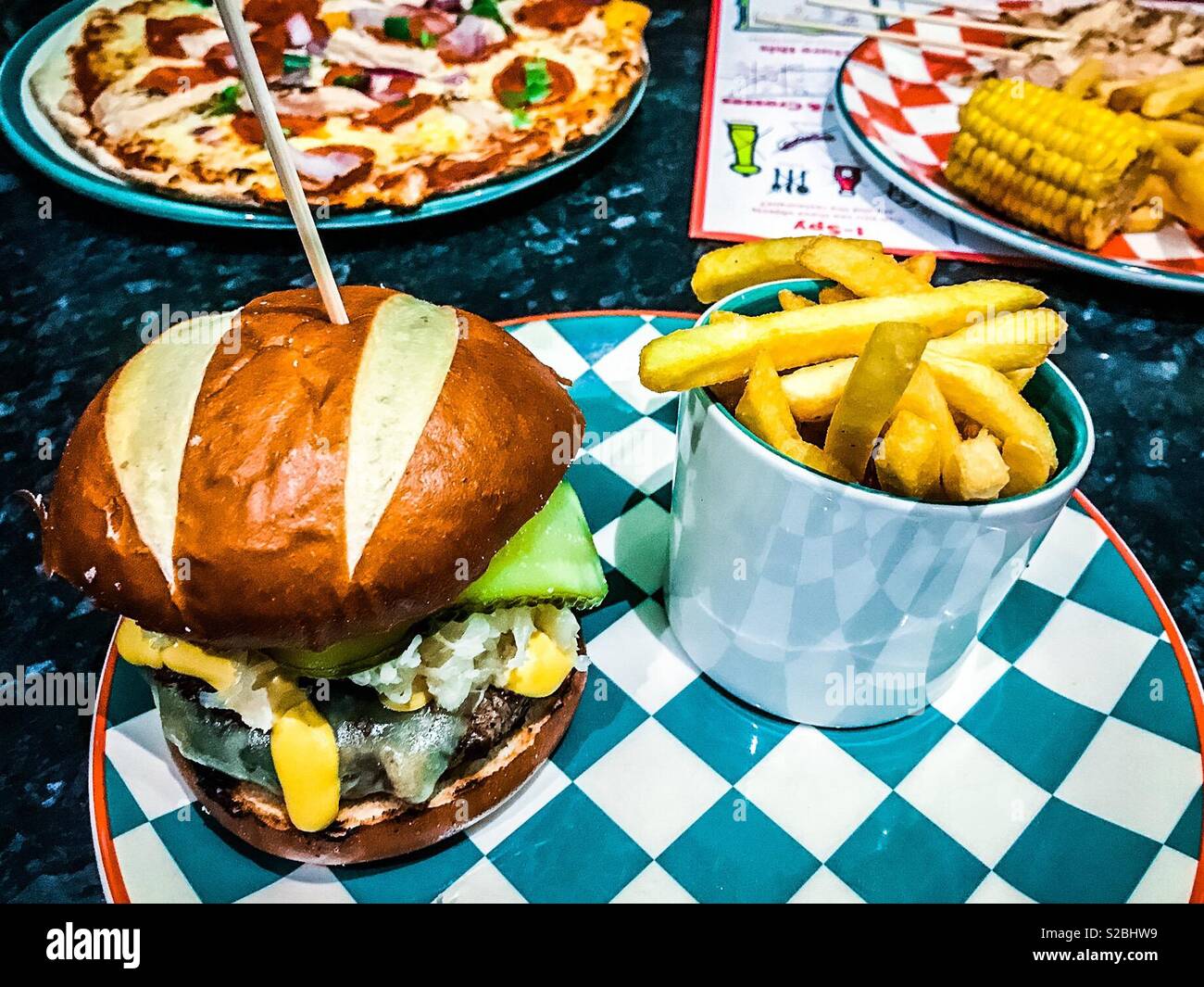 Sauerkraut and pickle cheeseburger and chips on patterned plate in a restaurant - Smartphone Captured Stock Image