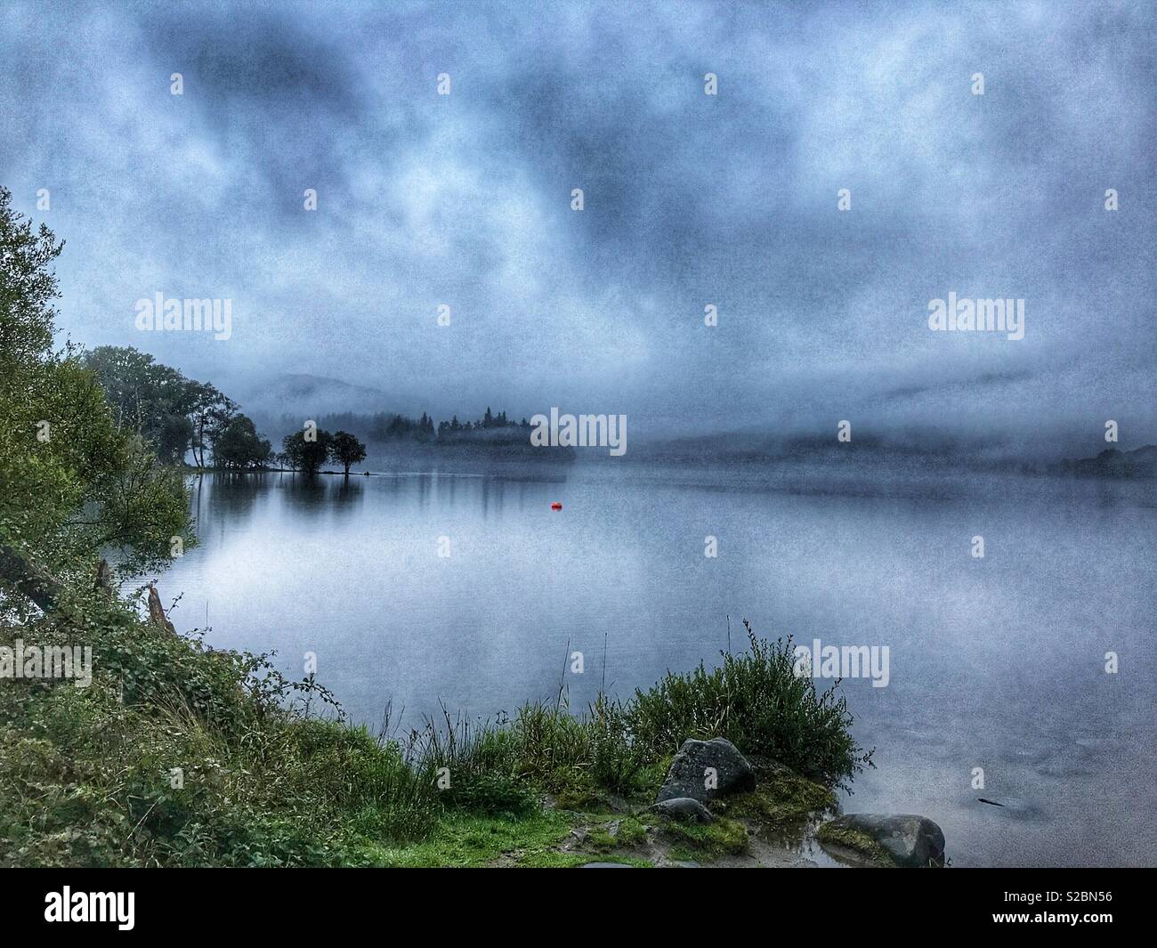 Early morning misty landscape view over a loch  in the Loch Lomond and The Trossachs National Park, Perthshire, Scotland - Smartphone Captured Stock Image