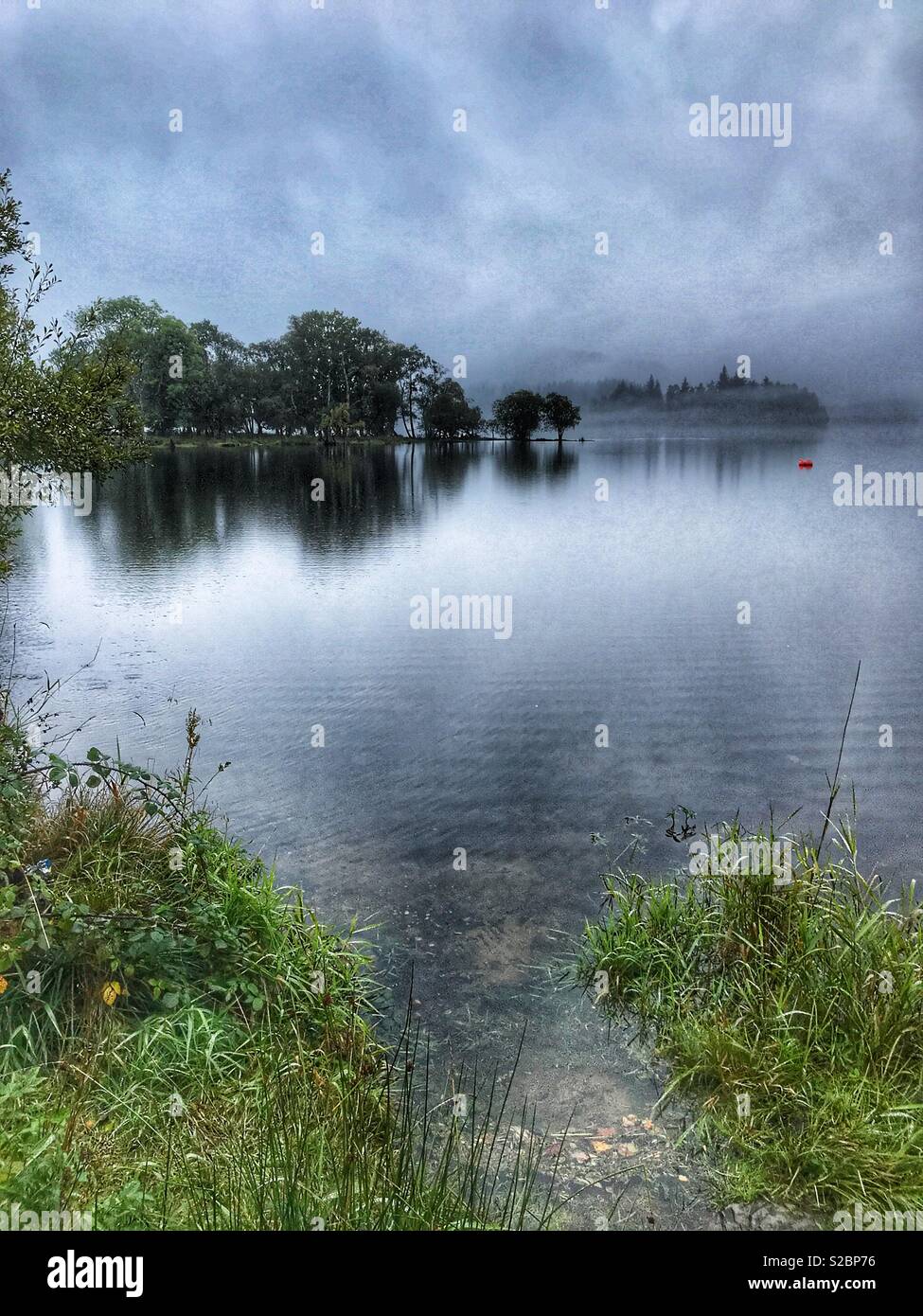 Early morning view of mist rising over a loch in Loch Lomond and The Trossachs National Park, Perthshire, Scotland - Smartphone Captured Stock Image
