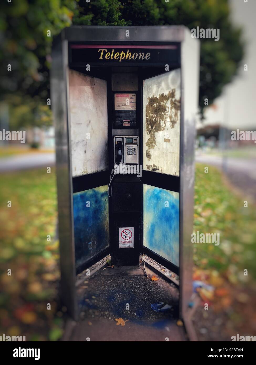 Shabby vandalised phone box on the outskirts of a city. Stock Photo