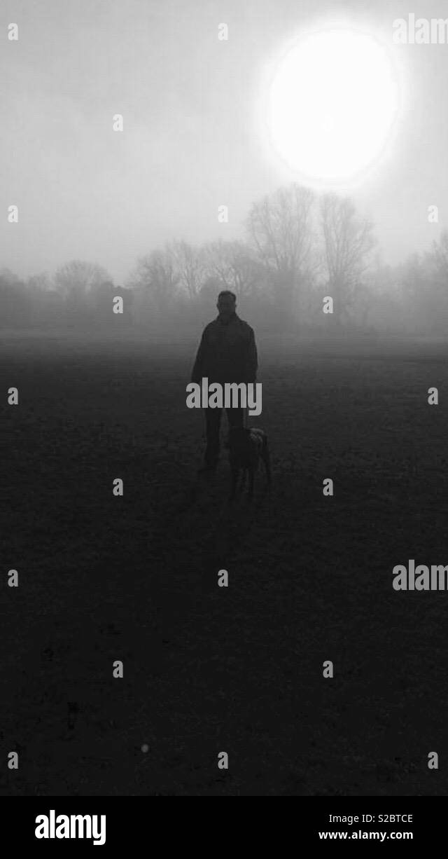 One man and his dog emerging from the fog early morning Stock Photo