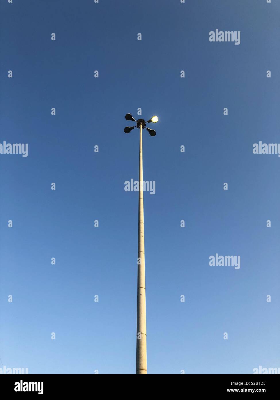 Light pole with only one light working, against a clear blue sky. - Smartphone Captured Stock Image