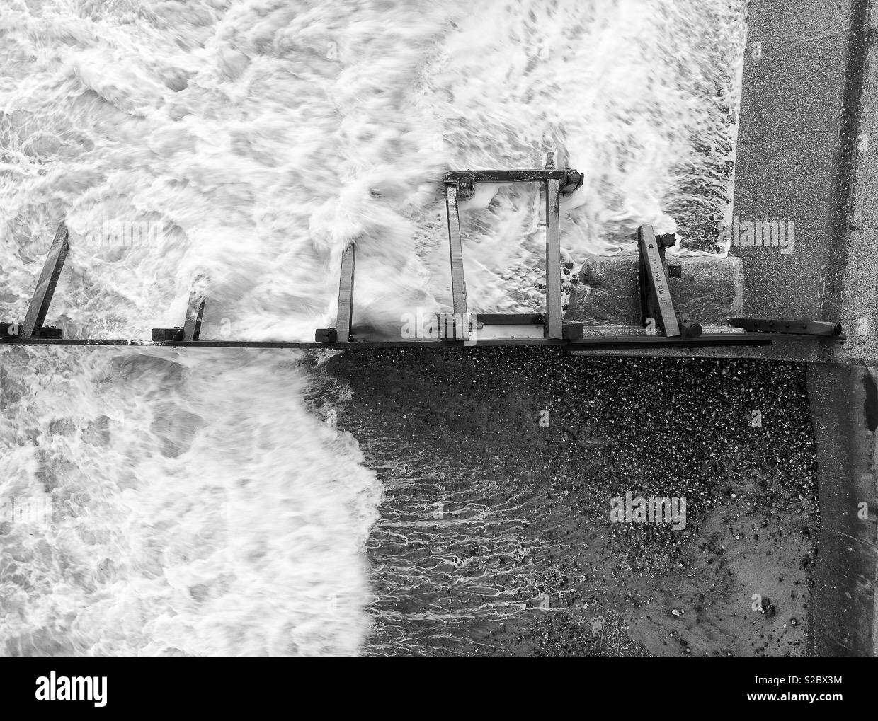 Incoming waves rushing along the beach against a sea wall. - Smartphone Captured Stock Image