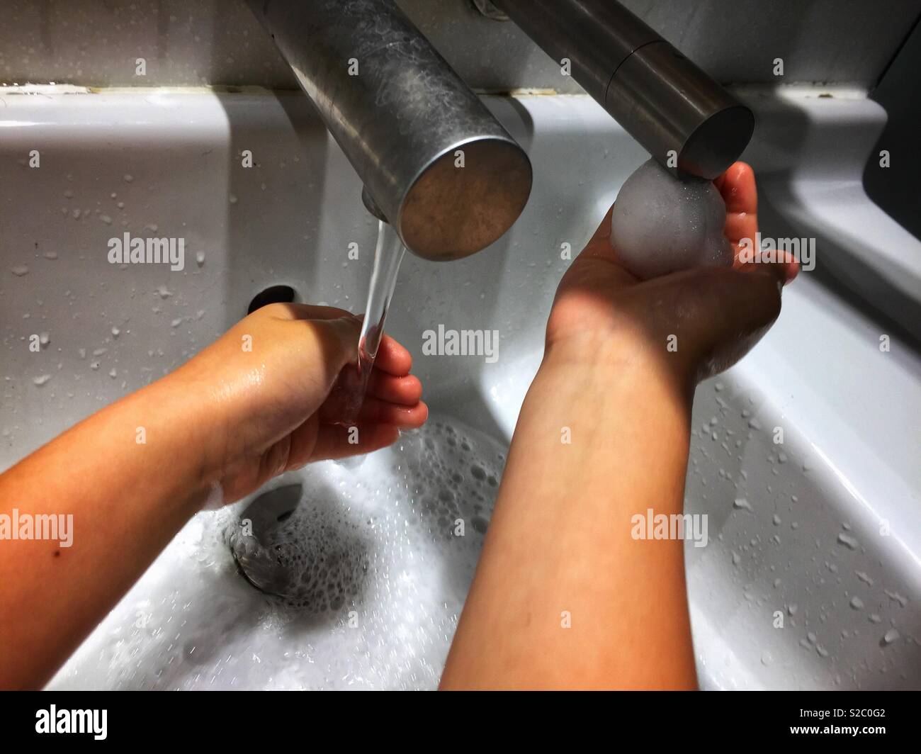 A child washes hands under a tap in a washroom. - Smartphone Captured Stock Image