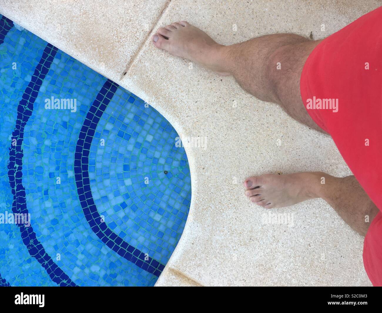 Man standing next to a swimming pool in red shorts - Smartphone Captured Stock Image