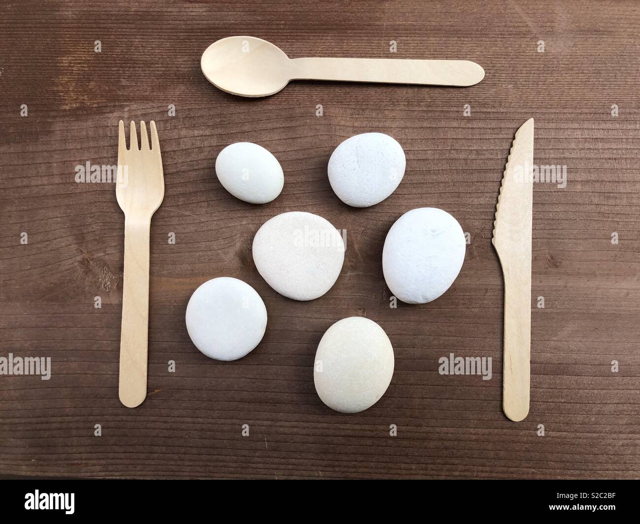 Meal time abstract concept with fork, spoon, knife and stones over wooden board - Smartphone Captured Stock Image