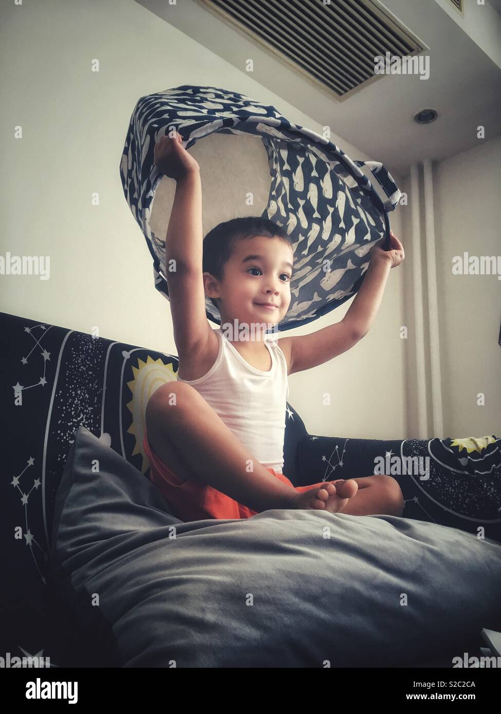 A boy playing by holding a basket above his head before put it over him. - Smartphone Captured Stock Image