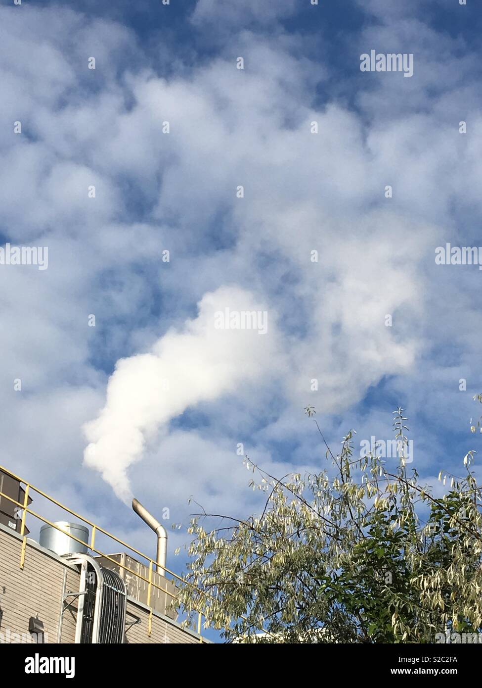 Carbon emissions remains a perpetual problem worldwide, but almost every nation is playing footsie with the problem, a factory spews out white smoke on a Sunday morning in Toronto. - Smartphone Captured Stock Image