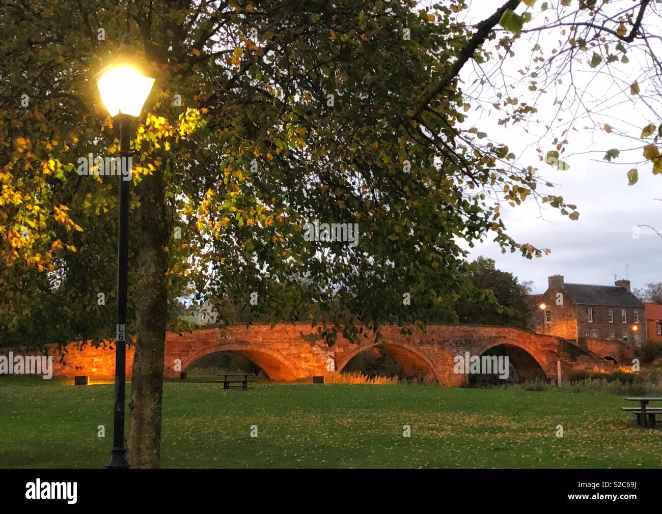 Historic arched Nungate Bridge lit up at twilight, Haddington, East Lothian, Scotland, UK - Smartphone Captured Stock Image