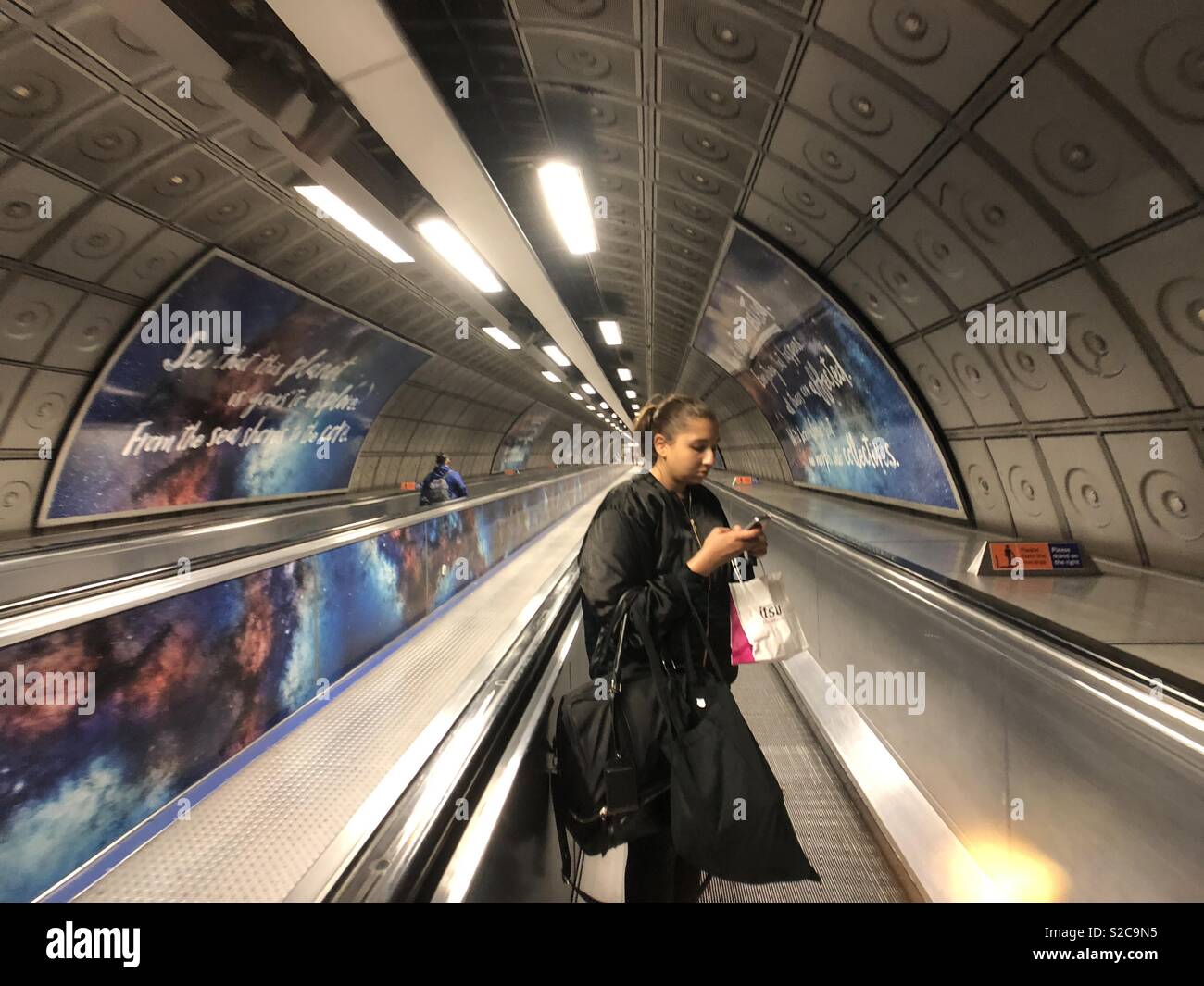 Woman checking phone on London Underground escalator late at night - Smartphone Captured Stock Image