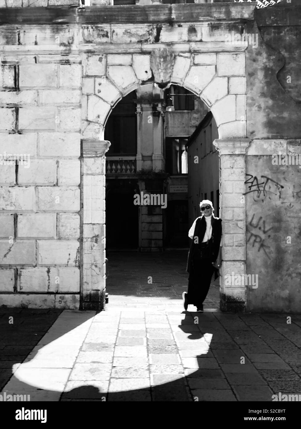 Black and white photo of a woman age 59 standing in stone archway in San Stephano Campo in Venice, Italy - Smartphone Captured Stock Image