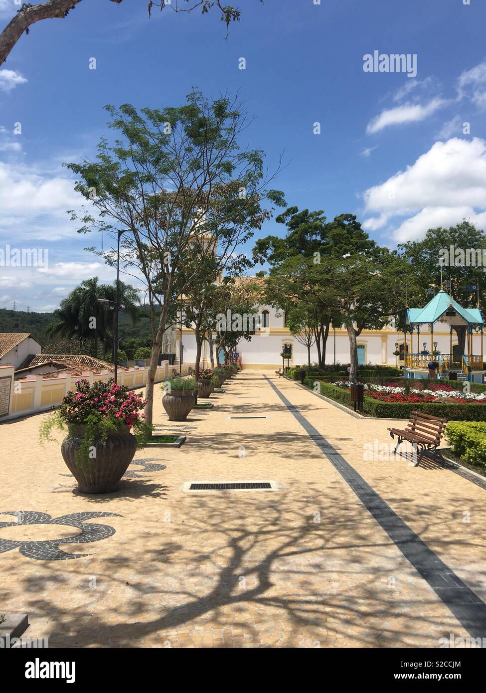 Santana de Parnaíba, a 1580 Brazil’s city. Church Square with spring flowers, park bank, bandstand, blue sky , trees and flowers glasses. Stock Photo