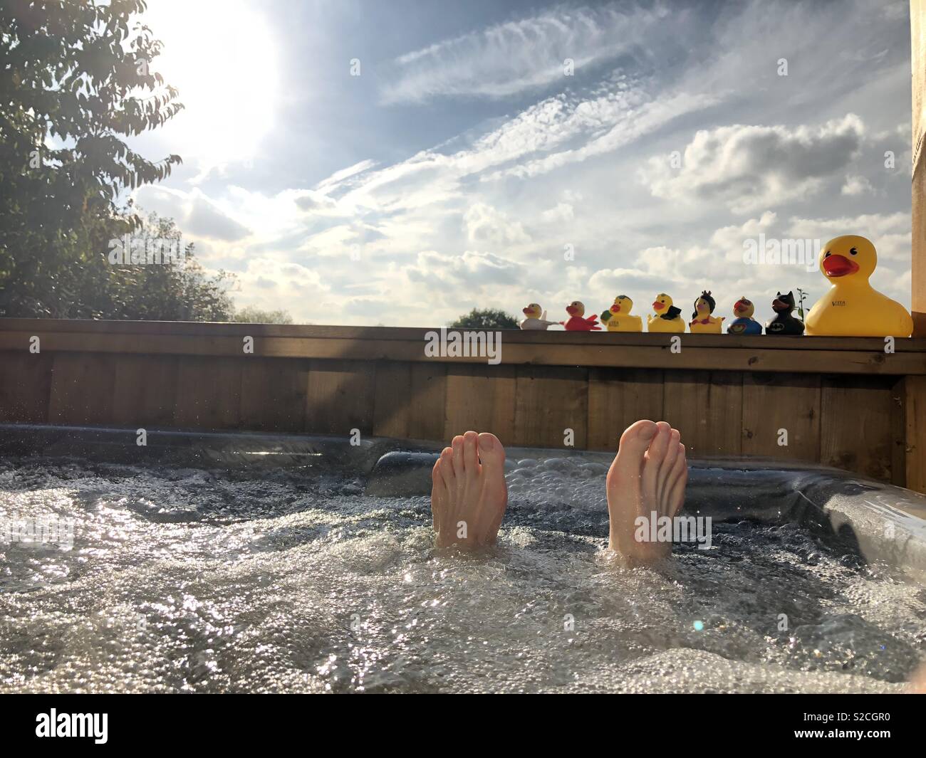 Feet and toes sticking out the hot tub on a sunny day with rubber ducks watching Stock Photo