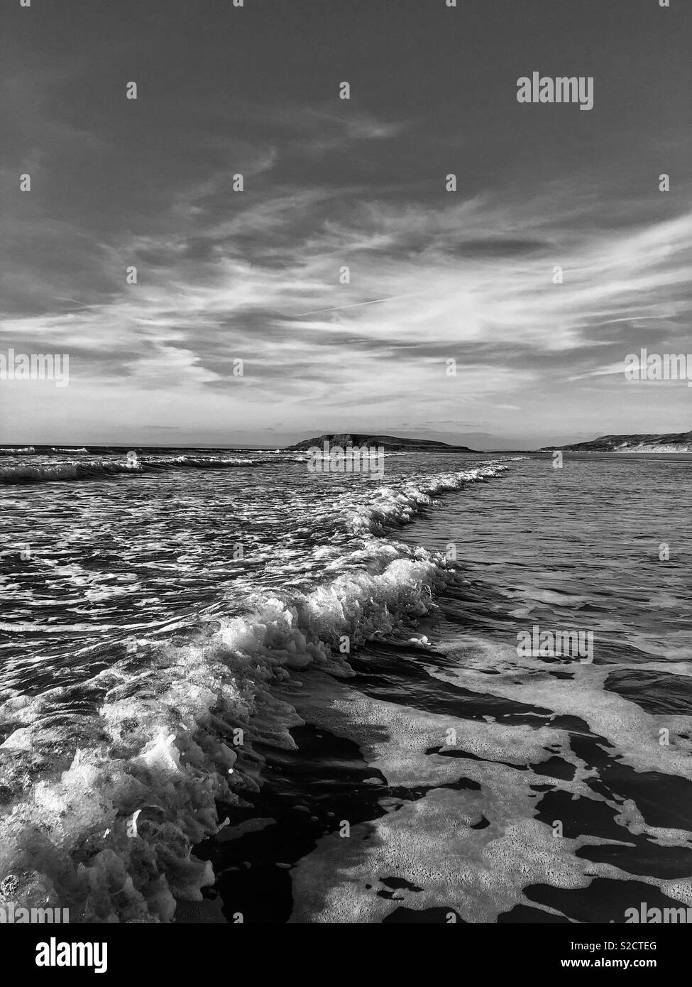 Wave breaking on Llangennith beach, Gower, Wales, October, with Burry Holms in the distance. Stock Photo