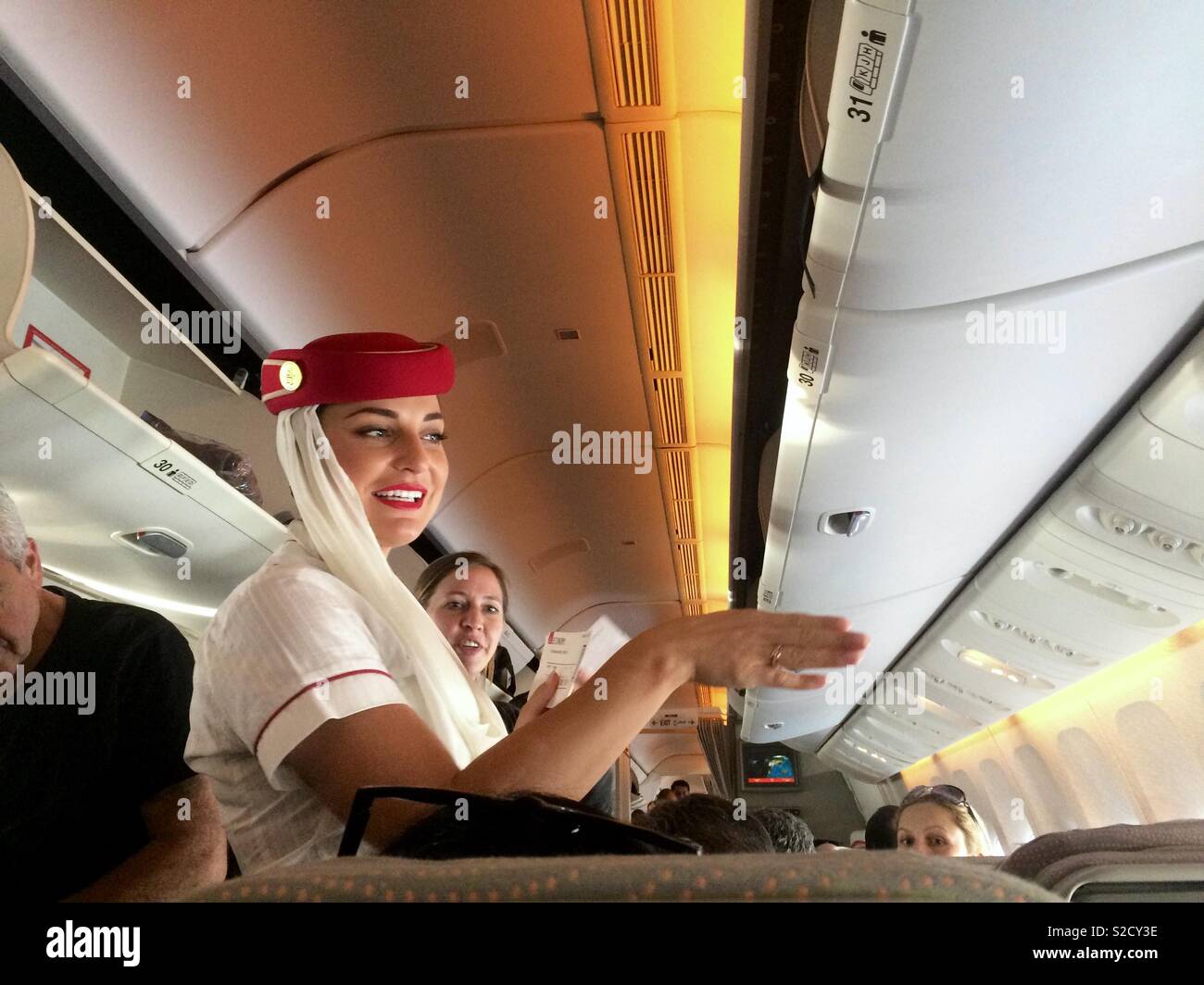 Emirates Airlines cabin crew assisting passengers in airplane before takeoff of aircraft Stock Photo