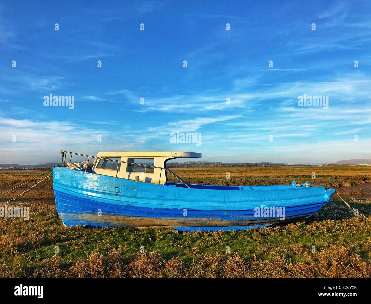 Old boat pulled ashore at Pen-clawdd, North Gower, Wales. Salt marshes can be see beyond. - Smartphone Captured Stock Image