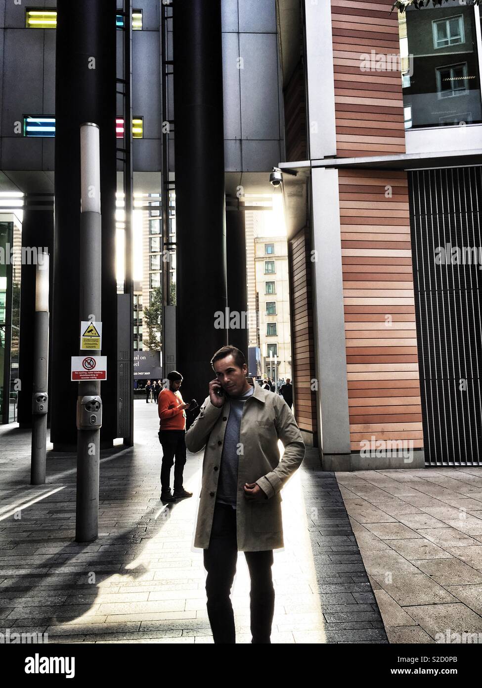 A man talks on the phone outside offices on Zoar Street in Southwark, London in England - Smartphone Captured Stock Image
