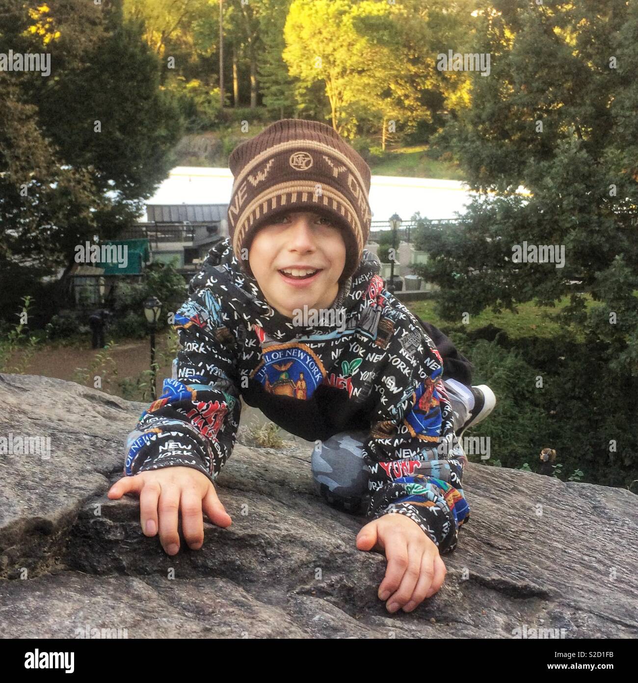 Nine year old boy rock climbing in Central Park, New York City, United States of America. - Smartphone Captured Stock Image