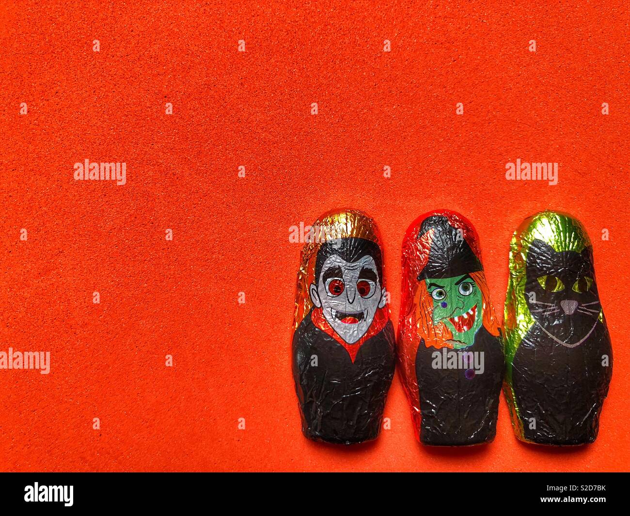 Three Halloween themed foil wrapped chocolates on a plain bright orange background with copy space - Smartphone Captured Stock Image