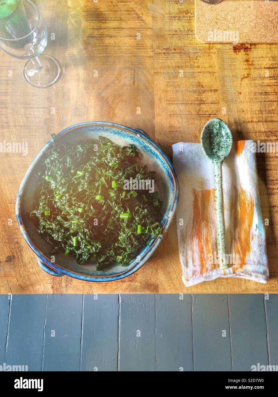 Cavolo Nero with garlic and butter in blue ceramic serving bowl with green dappled ceramic spoon and pretty napkin. On wooden table with copy space. Wine glass in top corner Stock Photo