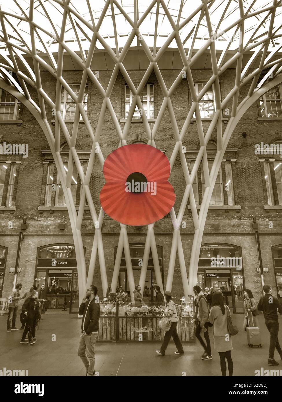 Giant red poppy memorial installation for Remembrance Day in kings cross st Pancras train station in sepia style black and white with red colour pop poppy Stock Photo