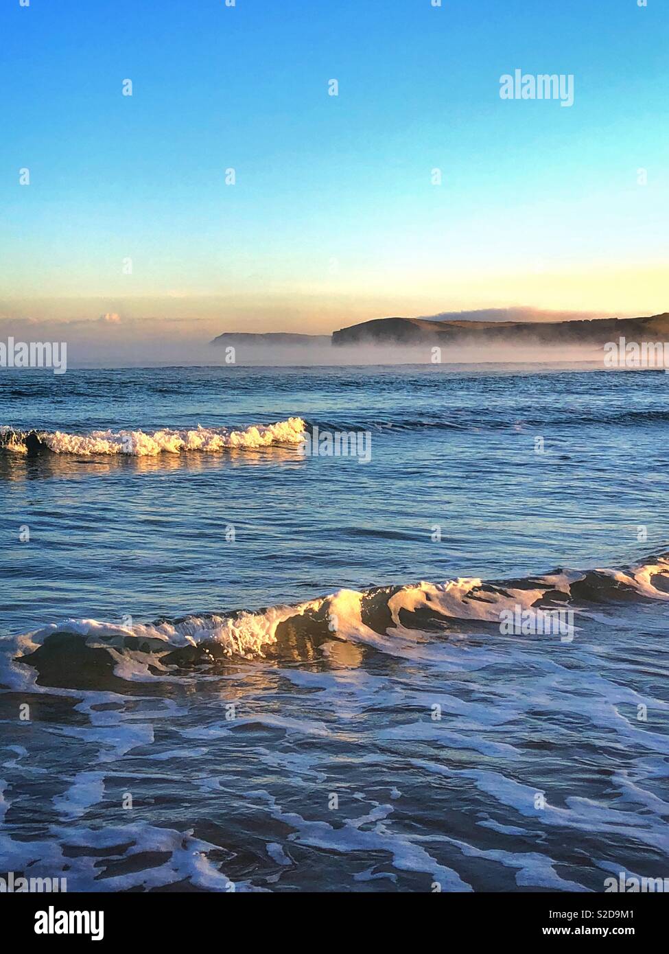 Early morning light on waves at Harlyn Bay with sea mist in the distance and Stepper point in the far distance, North Cornwall, England, October. Stock Photo