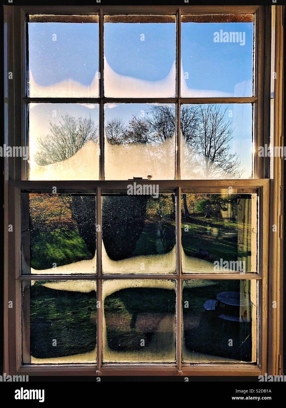 Autumn light shining through a traditional sash window on a cold morning in Scotland, with condensation visible and trees and blue sky outside. - Smartphone Captured Stock Image