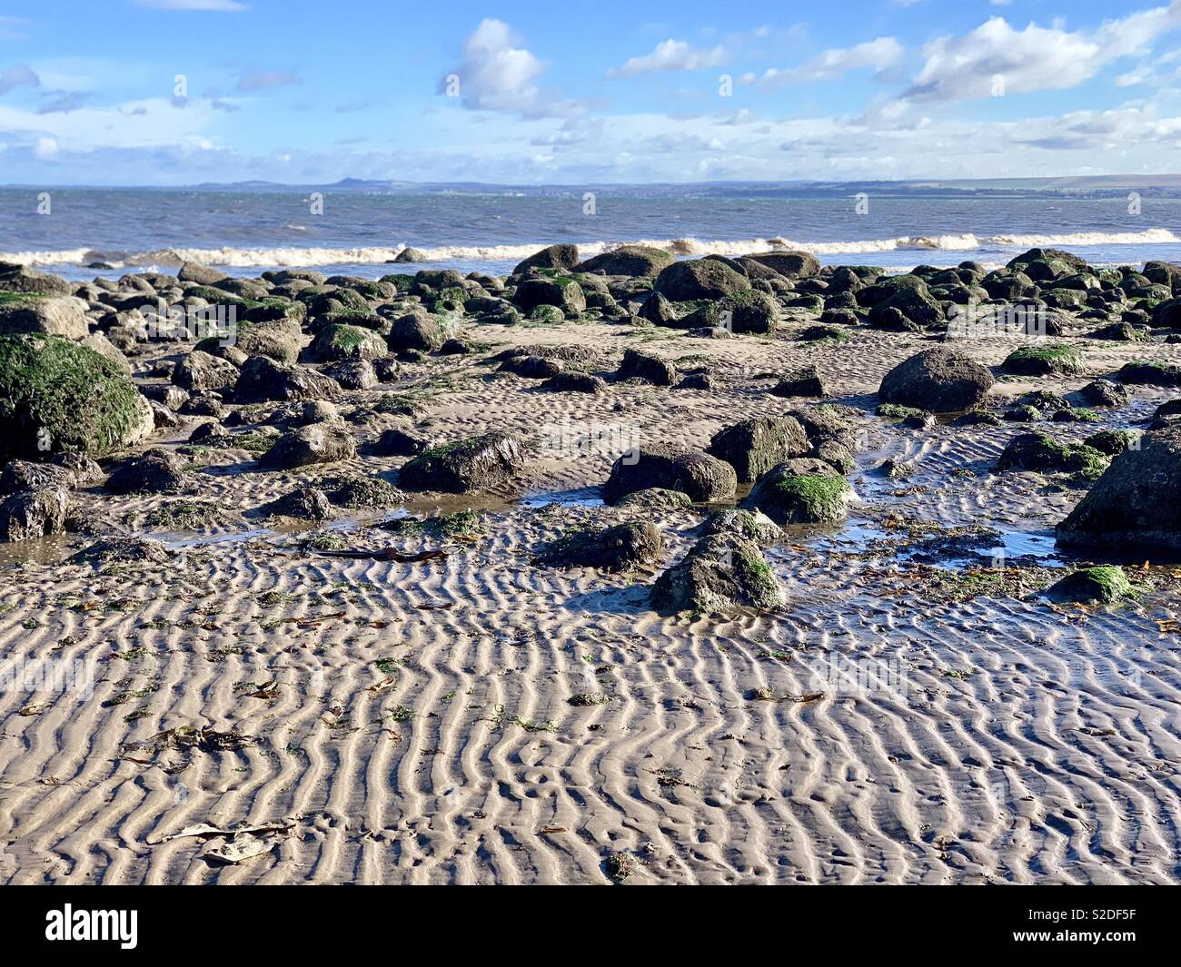 Receding tide exposes rocks on a beach in Edinburgh Stock Photo