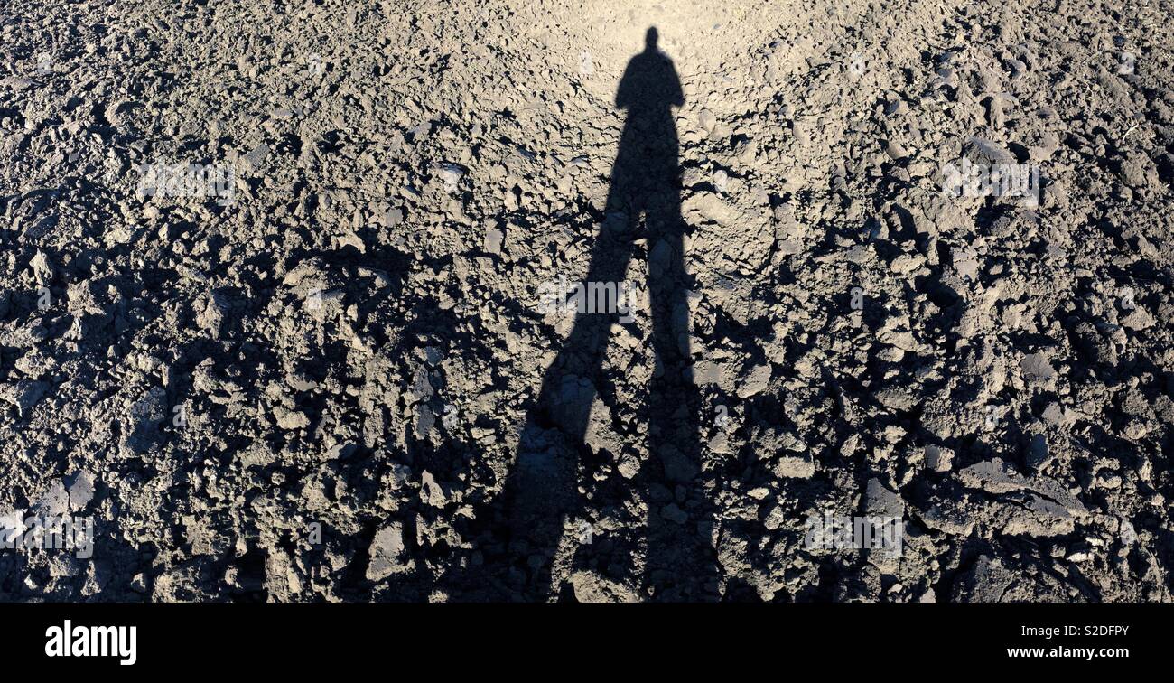 Silhouette of man against dark ploughed earth Stock Photo