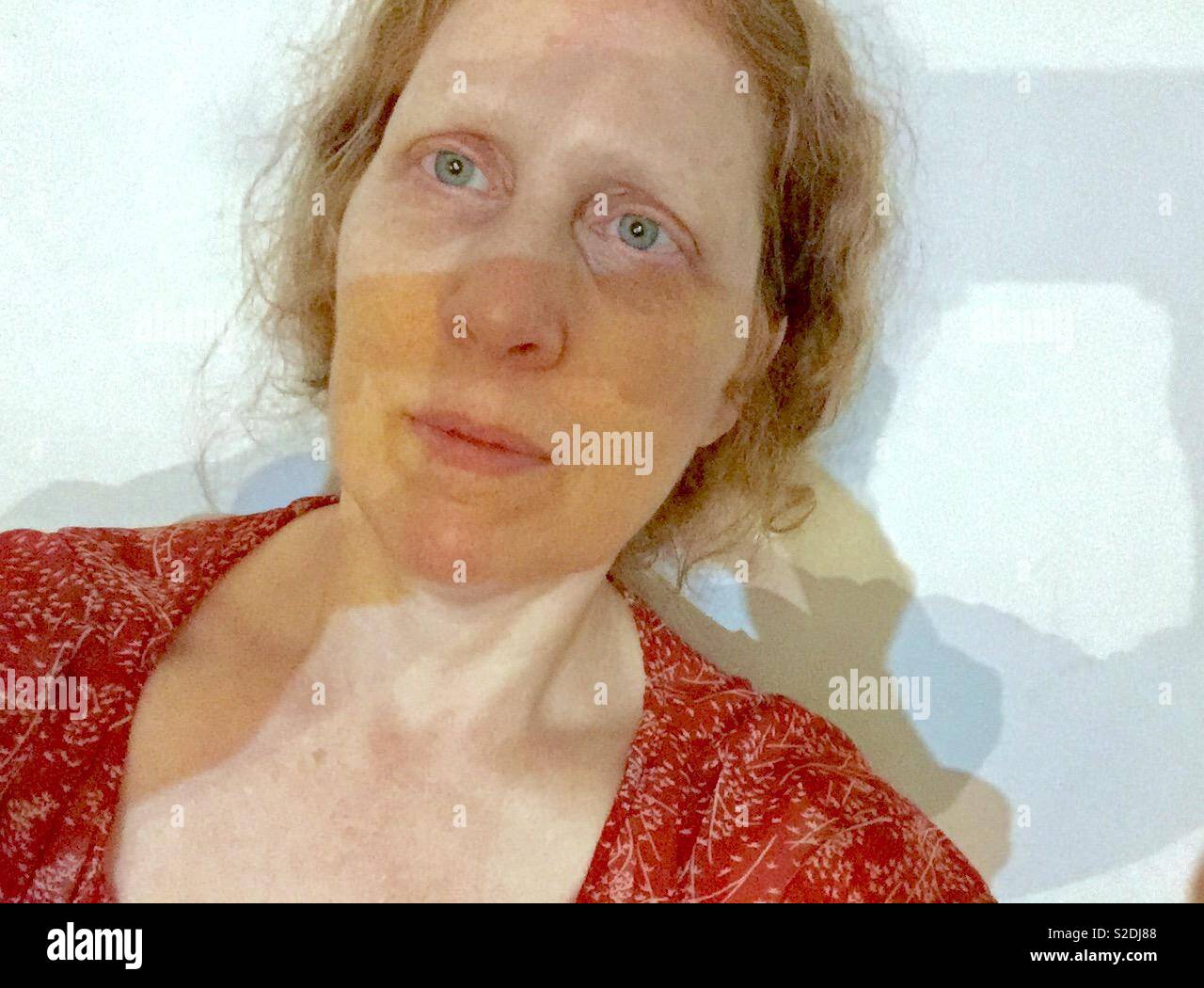 Red haired woman with freckles and light blue eyes taking a selfie against a white background. Stock Photo
