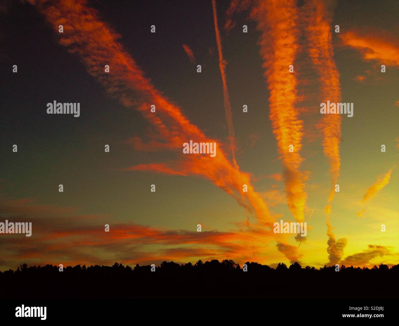 Fanned cloud formations and vapor trails glow in setting sun over farm field - Smartphone Captured Stock Image