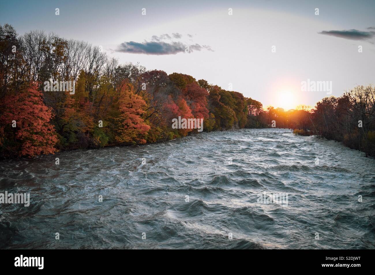 The colors of fall over a raging river at sunset Stock Photo