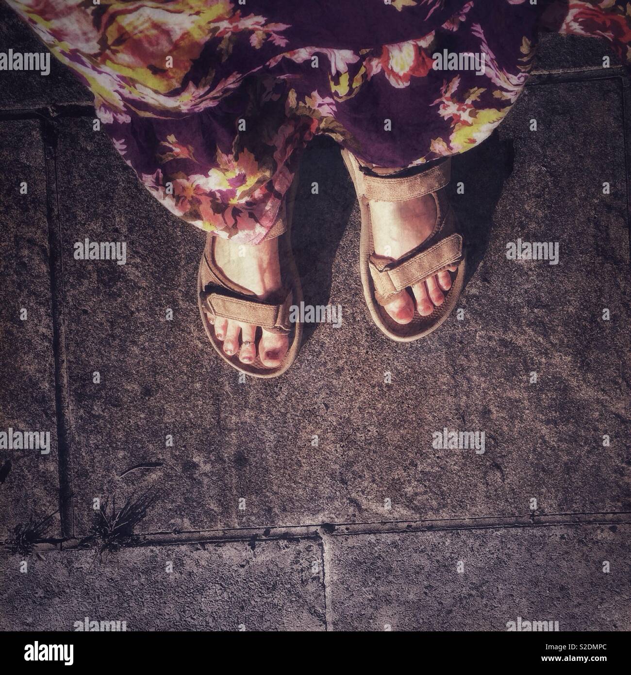 Sandalled feet of a woman in a long floor length floral sundress. Grunge, nostalgia. Stock Photo