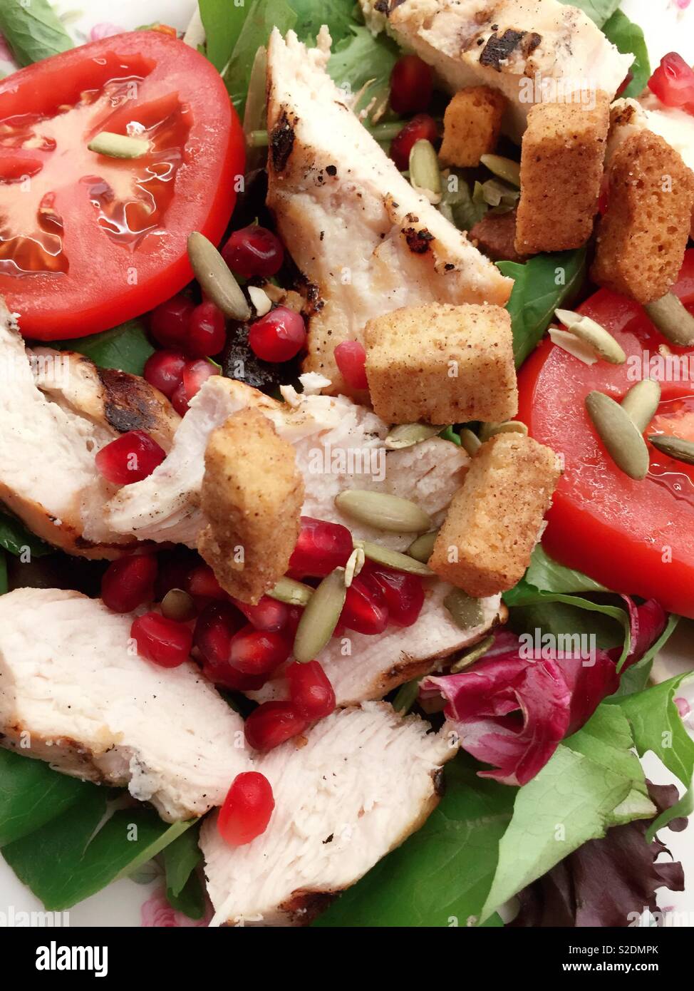 Close up of a nutritious autumn salad of pomegranate seeds, spinach, chicken pieces, tomato slices and freshly baked croutons, USAA - Smartphone Captured Stock Image